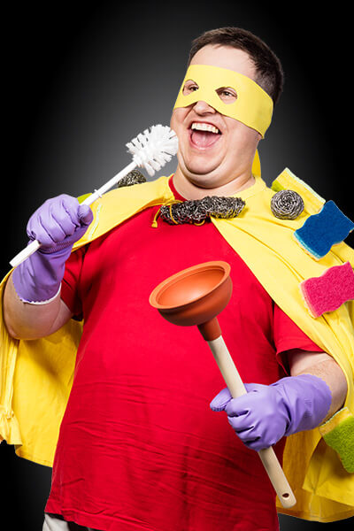 ein Mann mit gelber Maske und gelbem Umhang hält eine Klobürste und einen Pömpel in der Hand. Er sieht aus wie ein Superheld.