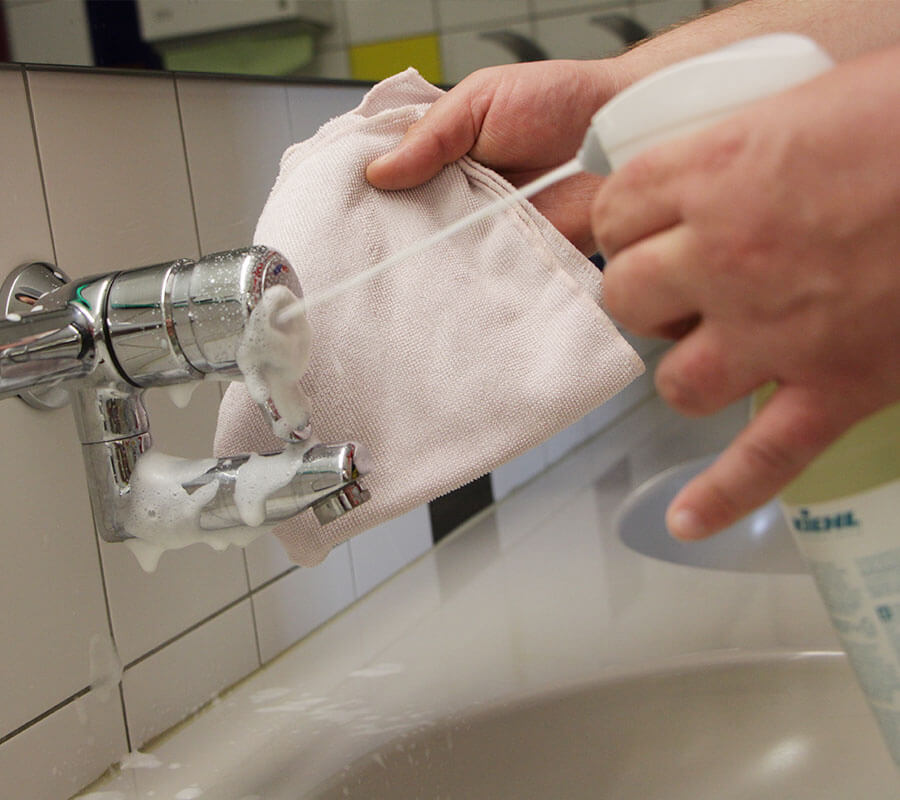 Hände beim Putzen einer Waschbecken-Armatur