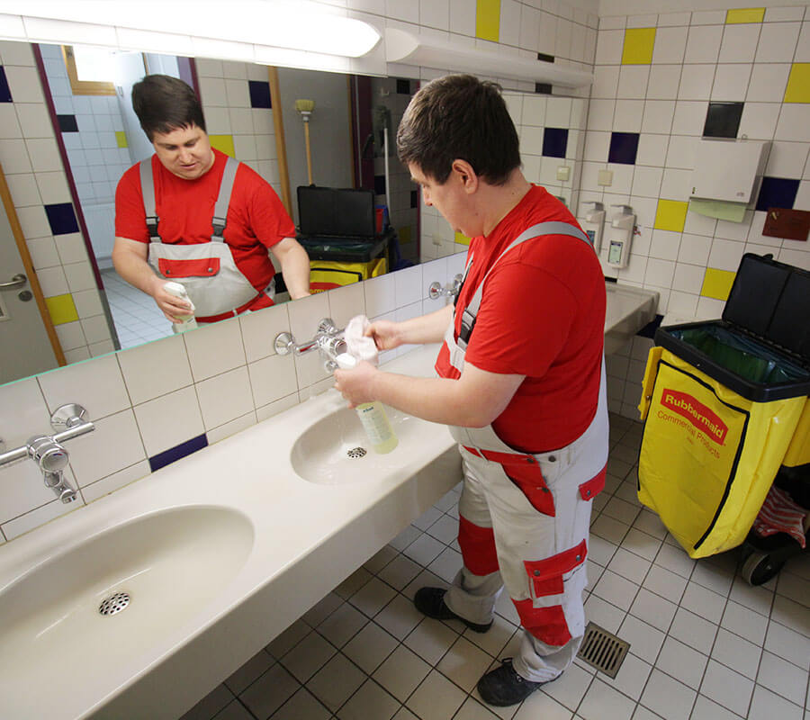 Junger Mann mit Spiegelbild putzt ein Waschbecken