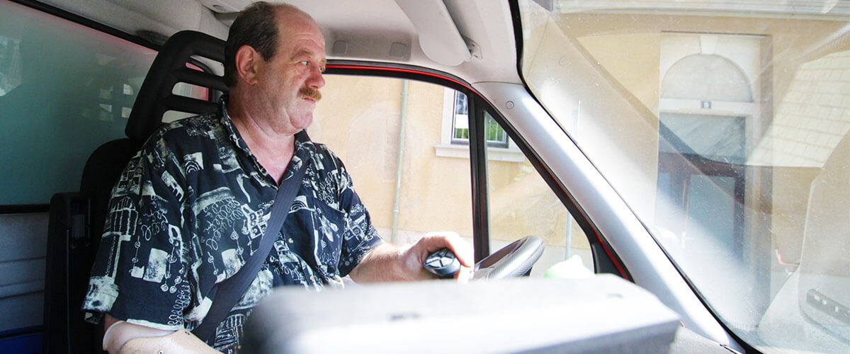 Portrait_Jobportal_Reinhard_02_1200x500 Mann mit Hakenhand am rechten Unterarm am Lenkrad seines LKW