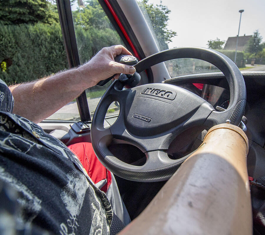 Mann mit Hakenhand am rechten Unterarm am Lenkrad seines LKW