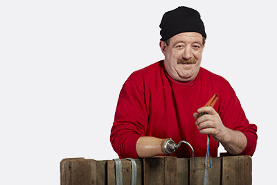 Portrait_Leistungen_Umzugs-und-Tranpsortservice_400x267 ein Mann mit einer Unterarmhakenprotese lehnt an einer Palette, er hat einen Spanngurt in der Hand